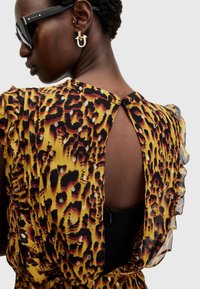 Robe à imprimé animal jaune avec des manches volantées, un dos ouvert et une doublure noire. Présente des accents métalliques et une fermeture à glissière cachée.