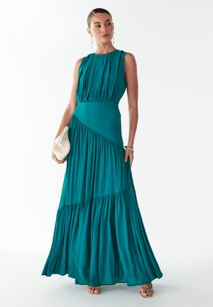 Maxi-jurk van teal stof met geplooide korset en gelaagde, vloeiende rok. Heeft een ronde halslijn en subtiele textuur. Gecombineerd met een geweven clutch.