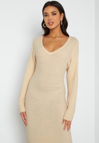 Abito in maglia a coste beige con scollo a V e maniche lunghe, caratterizzato da un corpino aderente e una gonna ampia, realizzato in un tessuto morbido.