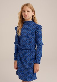 Blå mönstrad klänning med diamantmotiv. Långa ärmar, volangdetaljer vid axlar och ärmslut, elastisk halsringning och midjedetalj.