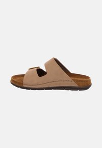 Beige mockasinsandalett med öppen tå, korsbanddesign, texturerad fotbädd och en brun gummisula. Har en guldfärgad spänne som accent.