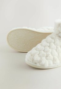 Witte pluizige slippers met een gestructureerd bovenwerk, voorzien van een bubbelontwerp en een rubberen zool met een sterrenpatroon in reliëf.