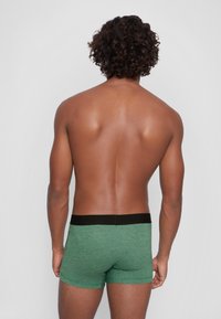 Grüne Boxer-Briefs mit strukturiertem Strickdesign und einem schwarzen elastischen Bund, von hinten betrachtet. Glattes Material und enganliegende Passform.