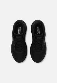 Zapatillas deportivas negras con una parte superior de malla, suela acolchada y diseño de cordones. Presentan un perfil elegante y detalles del logo en los laterales.