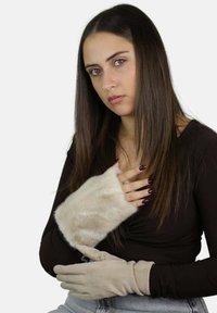 Beżowa opaska na nadgarstek z sztucznego futra i miękkie beżowe rękawiczki noszone razem, ukazujące teksturę i kontrastujące materiały. Modelka z długimi włosami.