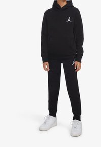 Completo di felpa e pantaloni neri realizzato in tessuto morbido, con cappuccio, tasca a marsupio e accenti bianchi del logo Jordan. Indossato con sneakers bianche.