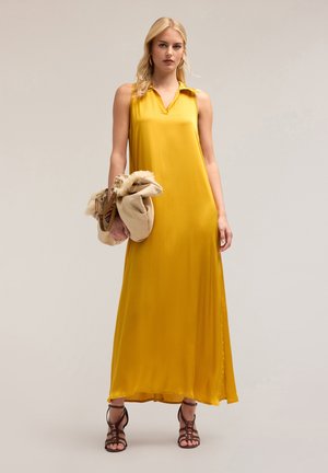 Abito maxi giallo senza maniche con colletto, texture liscia e spacco laterale. La modella tiene una borsa beige con dettagli in pelliccia.