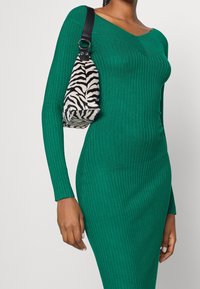 Zelené žebrované pletené šaty s dlouhými rukávy a výstřihem do V. V páru s kabelkou se zebřím vzorem a černým popruhem.