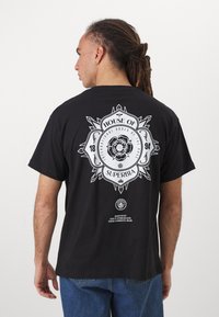 Tricou din bumbac negru cu un design grafic mare, alb, pe spate, care include text, elemente florale și accente geometrice.