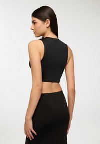 Czarny krótki top na ramiączkach wykonany z gładkiego, elastycznego materiału, z okrągłym dekoltem i bez rękawów, w połączeniu z czarną spódnicą.