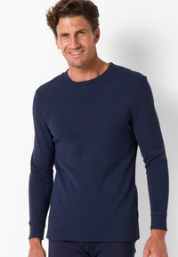 T-shirt a maniche lunghe blu navy realizzato in morbido cotone, con collo a giro e maniche con polsini, caratterizzato da una silhouette aderente e spacchi laterali.