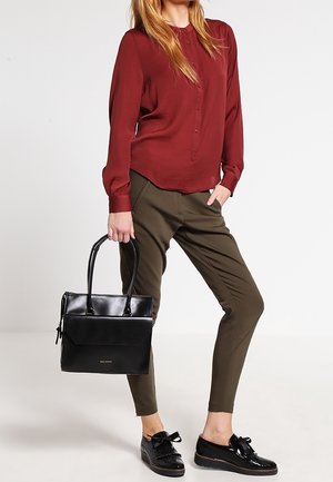 Chemise bordeaux à manches longues, pantalon olive ajusté, sac à main noir avec poignées supérieures et chaussures noires avec détail nœud. Textures lisses.