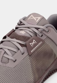 Lys lilla træningssko med mesh-overdel, flade snørebånd og gummidetaljer med et mønstret design og forstærket hælområde.