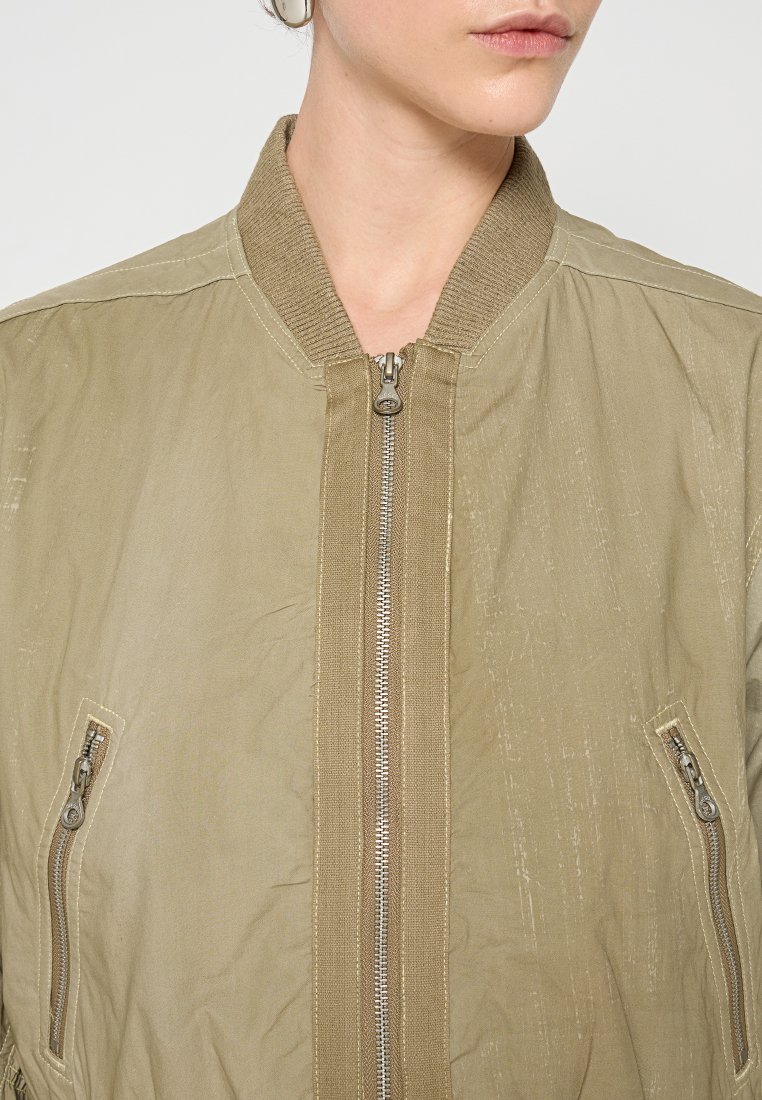 Khakifarbene Bomberjacke mit geripptem Kragen, vorderem Reißverschluss und seitlichen Taschen. Der Stoff hat einen sanften Glanz und eine strukturierte Oberfläche.