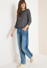 Czarnobiały wzorzysty top z długim rękawem, jasnoniebieskie dżinsy z denimu i beżowe trampki. Strój cechuje się luźnym krojem i subtelnymi detalami.