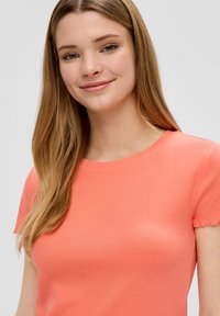 Korte mouwen, geribbelde t-shirt in een heldere koraalkleur, met een ronde halslijn en iets rafelige mouwranden. Zachte stoffen textuur.