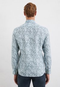 Camicia button-up azzurra chiara con motivo floreale, maniche lunghe e colletto, con piccoli dettagli gialli sui bottoni.