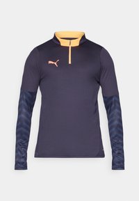 Sötétkék, hosszú ujjú sportpoló narancs színű félcipzárral, textúrált kék ujjakkal, melyek finom mintázattal rendelkeznek, és a mellkasán egy logó található.