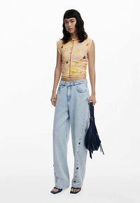 Krátky top s kvetinovým vzorom v broskyňových tónoch, doplnený voľnými svetlomodrými džínsami so zapínaním na bočných gombíkoch a námorníckou kabelkou.