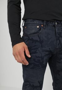 Mörka denimjeans med mönster i kamouflage, med kopparfärgade detaljer och slim fit. Matcher med en svart långärmad tröja.