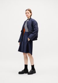 Vadderad marinblå jacka med orange foder, randig topp och knälång texturerad kjol. Svarta loafers med kraftiga sulor och ankelstrumpor.