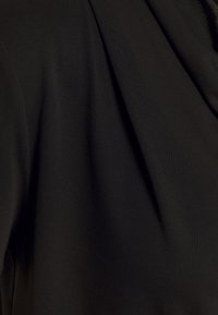 Svart tyg med en slät textur och en subtil lyster, med drapering och mjuka veck som förmedlar en lätt och flödande utseende.