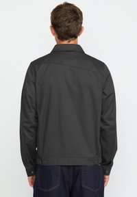 Donkergrijze jas met een kraag, lange mouwen en zichtbare stiksels. Heeft een rechte snit en knoopmanchetten. Minimalistisch ontwerp.