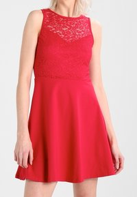 Czerwona sukienka z koronkowym gorsetem i gładką spódnicą. Bez rękawów, w kształcie rozkloszowanym, z widoczną teksturą i ozdobami w górnej części.