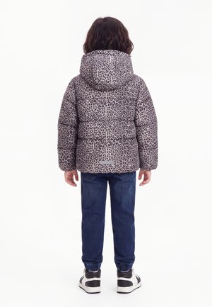 Kind steht mit dem Rücken zum Betrachter, trägt eine Kapuzenjacke mit Leopardenmuster, dunkelblaue Jeans und weiße sowie schwarze Sneakers.
