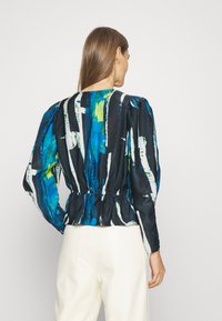 Svart topp med en färgglad abstrakt tryck i blått, grönt och vitt. Designen inkluderar puffärmar och en rynkad midja.