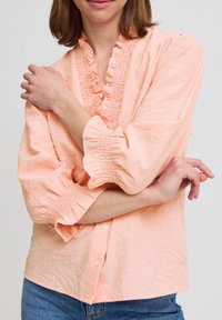 Peach striped blouse with ruffled neckline and smocked cuffs. Button-down design with lightweight, textured fabric. Fitted at the waist.