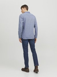 Camisa de franela azul con cuello, puños abotonados y una tela texturizada. Llevada con jeans oscuros y botas de tobillo marrones.