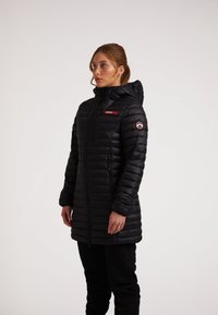 Giacca a vento nera lunga con cappuccio, design trapuntato orizzontale, chiusura con zip e accentuazione rossa sul petto; presenta una patch con logo sulla manica.