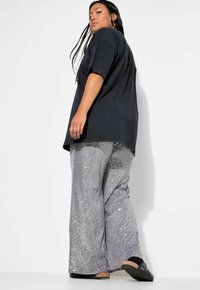 T-shirt nera oversize a maniche corte abbinata a pantaloni larghi in paillettes argento, con una texture liscia e design a gamba larga.