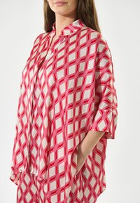 Röd och vit mönstrad blus med ett geometriskt diamantmönster, lätt material, loose fit och krage med knappar samt korta ärmar.