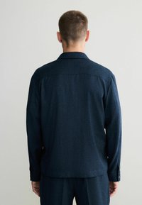Camicia a maniche lunghe blu scuro realizzata in un tessuto testurizzato, con colletto classico e polsini abbottonati, vista dal retro.
