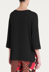 Maglietta nera a maniche lunghe con una vestibilità rilassata e un ampio scollo. Tessuto morbido e cuciture laterali con spacco, abbinata a pantaloni rossi con fantasia.