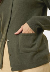 Olivově zelený cardigan s jemnou texturou, s přírodními knoflíky, žebrovanými manžetami a přední kapsou. Lehký a navržený pro pohodlí.
