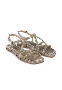 Sandali metallici dorati con suola piatta, punta quadrata e cinghie incrociate arricchite da piccole strass. Include una cinghia regolabile alla caviglia.