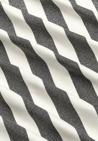 Černobílá tkanina s vzorem zigzag, obsahující texturované šikmé pruhy na hladkém pozadí, vytvářející vlnitý vzhled.