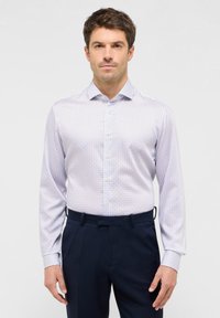 Camicia bianca con un sottile motivo geometrico blu, colletto button-down e maniche lunghe, abbinata a pantaloni navy scuri.