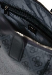 Interior de bolso negro con patrón, bolsillo con cremallera, forro suave y detalles con el logo. Presenta herrajes plateados y bordes estructurados.