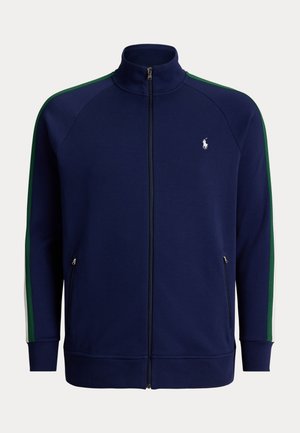 Granatowa kurtka sportowa na suwak z zielonymi i białymi paskami na rękawach, stójką, przednimi kieszeniami na zamek i białym logo gracza polo na piersi.