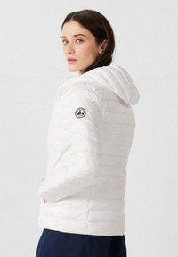 Witte donzen jas met capuchon, voorzien van een doorgestikt ontwerp en zijzakken. Logo-patch op de linker mouw voegt detail toe.