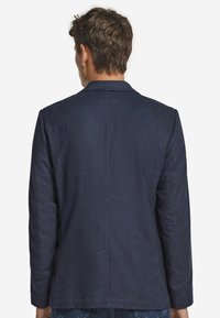 Marinblå kavaj med skräddarsydd passform, med spetsig krage, långa ärmar och en slät yta. Inkluderar diskret sömnad och sidofickor.