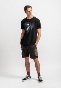Zwart t-shirt met een ruimte-thema graphic in levendige kleuren. Gecombineerd met olijfkleurige cargoshorts, zwarte sneakers en kleurrijke sokken.