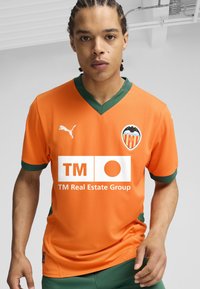 Oranžový futbalový dres s zelenými akcentmi, ktorý má výstrih do V, logo Puma a sponzorské označenie vpredu a na ľavej hrudi.