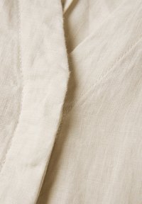 Tessuto in lino color crema con una sottile texture e una leggera lucentezza, caratterizzato da delicati punti di cucitura e una piega drappeggiata.