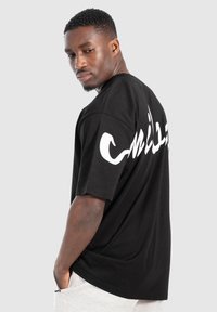 Camiseta negra de gran tamaño en tejido de algodón con mangas cortas. Logo blanco impreso notable en la parte posterior, ajuste relajado y textura suave.