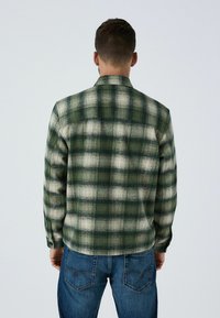 Zaļi un balti svītrota krekls ar mīkstu tekstūru, garām piedurknēm un smailu apkakli, saskaņots ar ziliem džinsiem.